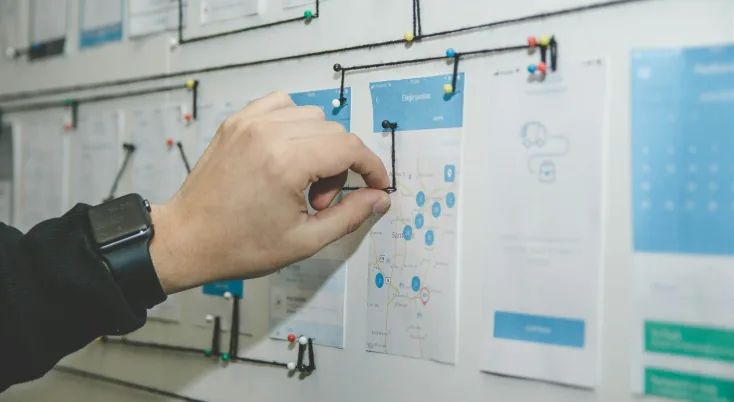 Hand pinning printed app wireframes connected by string on a planning wall